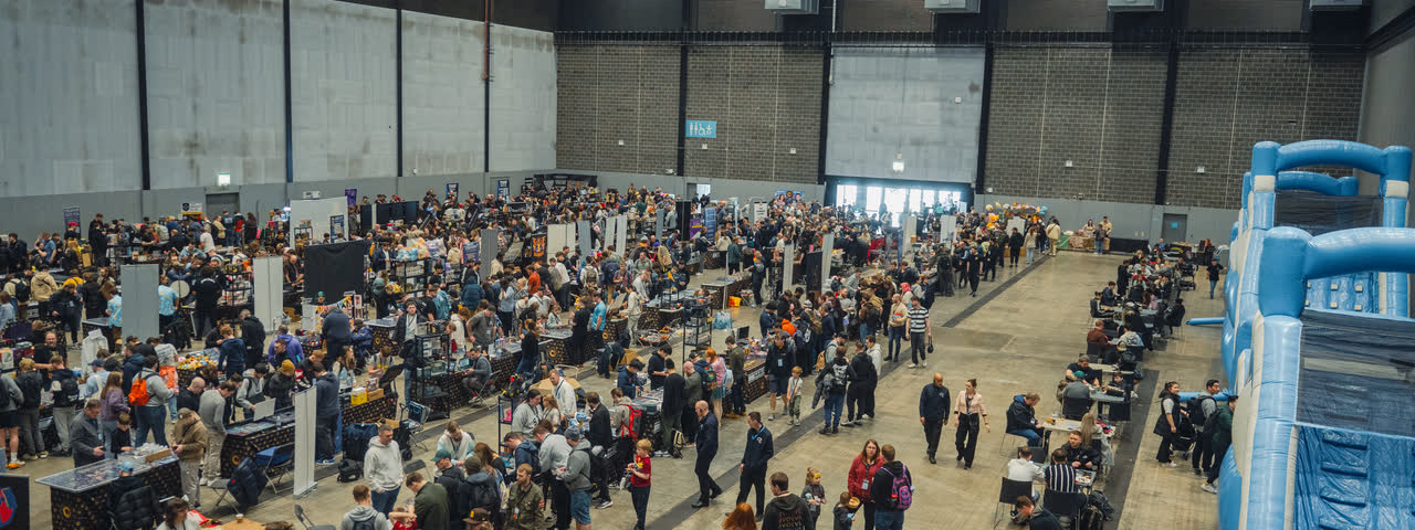 The main aisle seen end to end, packed with people either side of the trading tables.