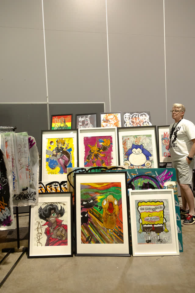 Framed pop-art prints leaning against a wall at an artist stand.