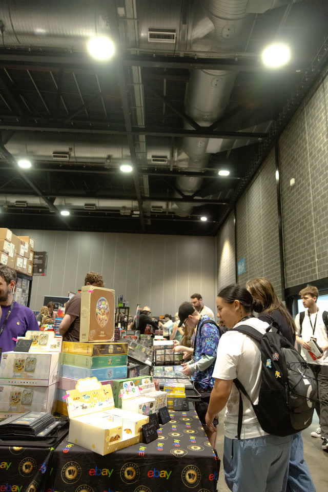 A crowded stand of sealed boxes, collectors lined up along it under the ceiling lights.