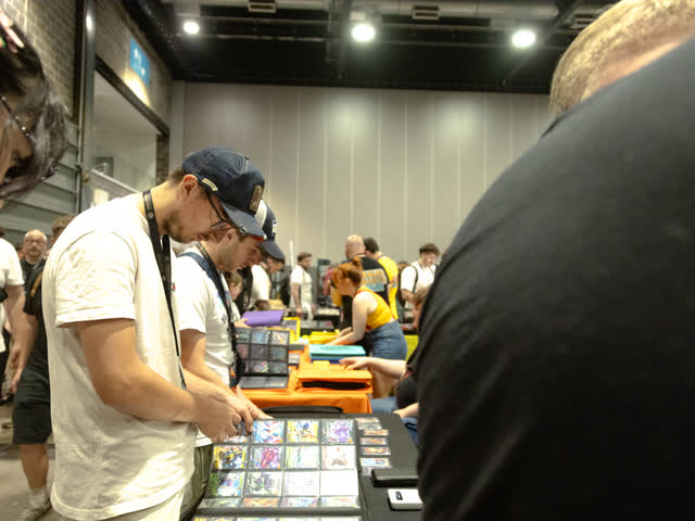 A collector in a cap flicking through a binder at the edge of a busy table.