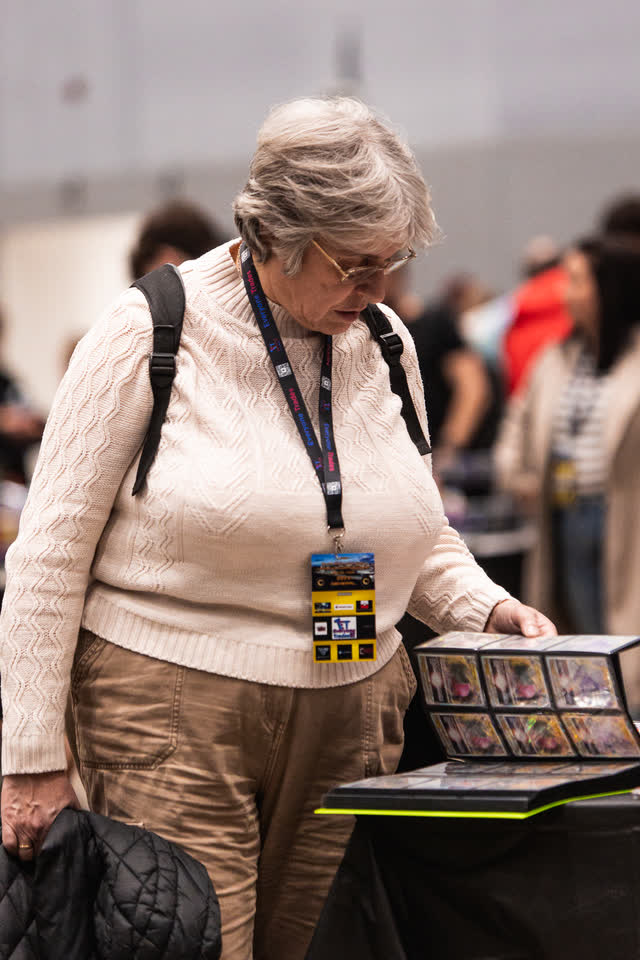 An older woman leaning over a table to look through a binder of cards.
