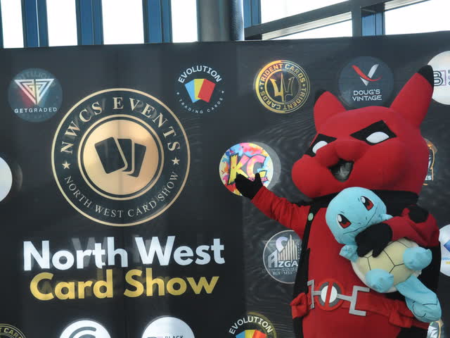 A mascot holding a Squirtle plush in front of the North West Card Show backdrop.