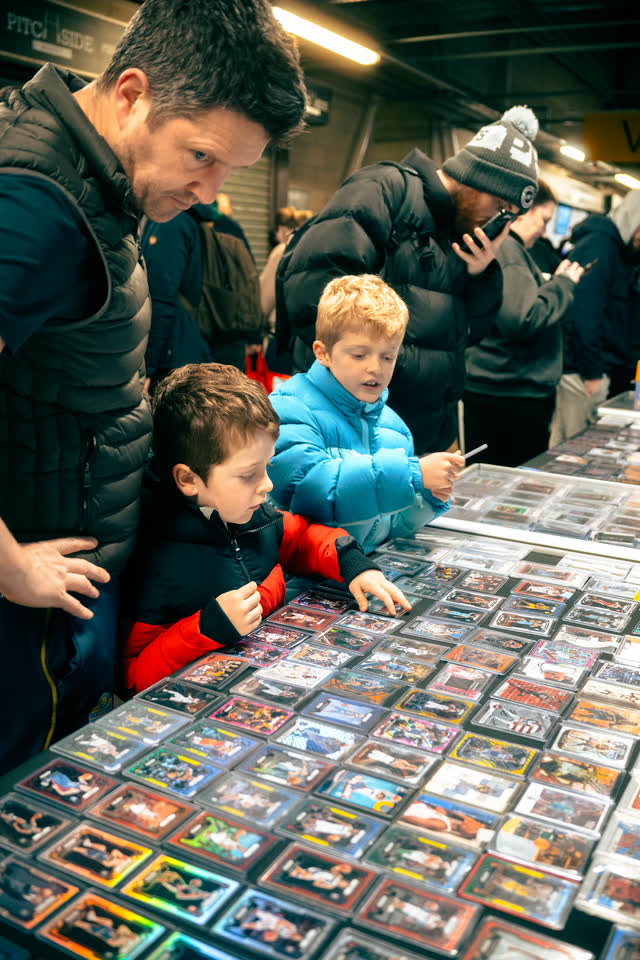 A father and two children leaning over a table covered in sleeved cards.