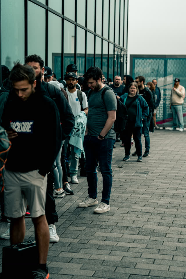 Collectors waiting in line outside the venue, the glass wall stretching away beside them.