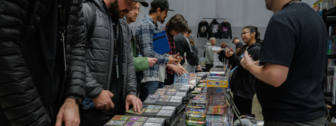 A long table of binders with collectors browsing along it and a trader serving across.