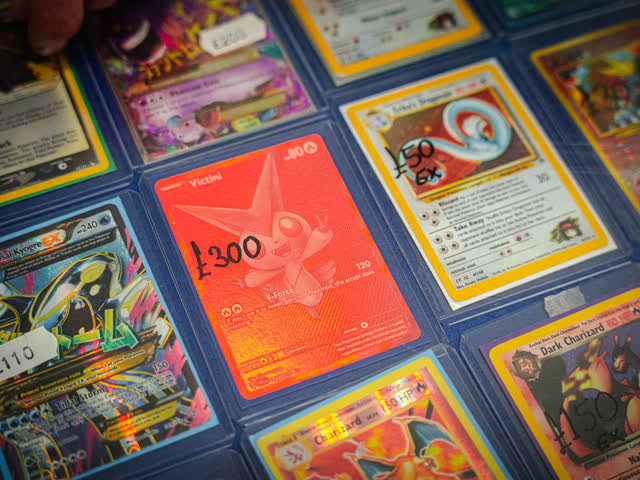 Vintage holographic Pokemon cards with handwritten price tags on a display.