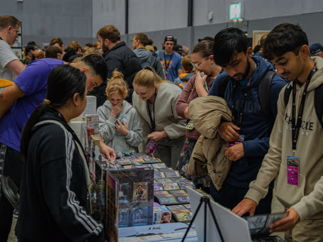 A table three deep with collectors leaning in over binders and boxes.