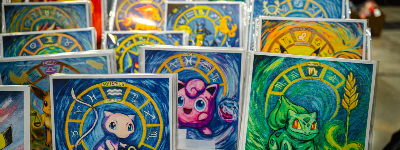 Painted Pokemon artworks in bright frames lined up at an artist stand.