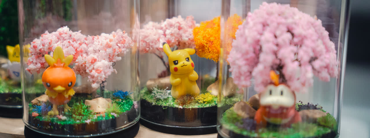 Handmade terrariums in glass domes, each with a small Pokemon figure under a blossom tree.