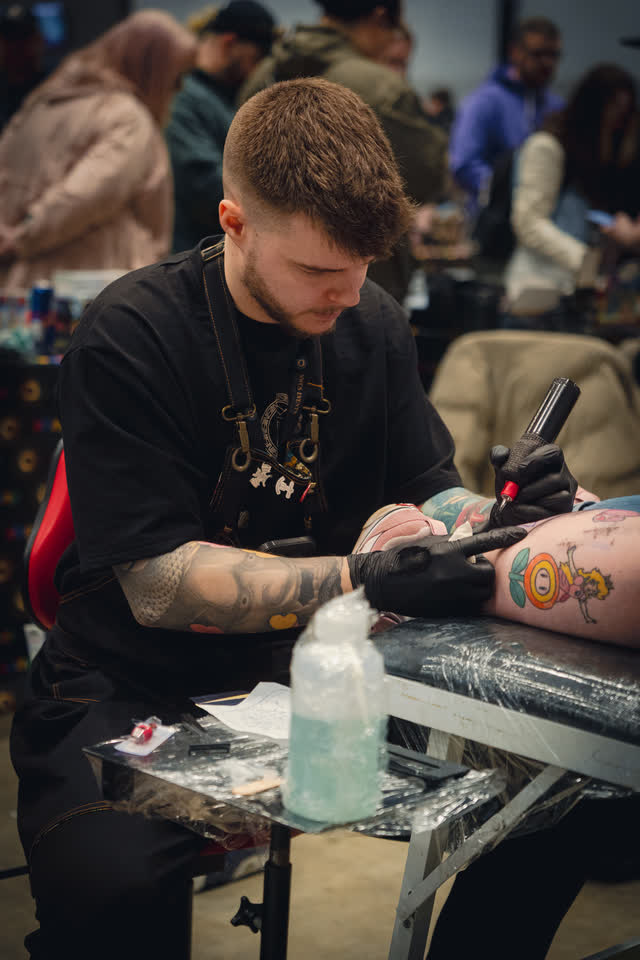 A tattoo artist working on a customer arm at his station on the floor.