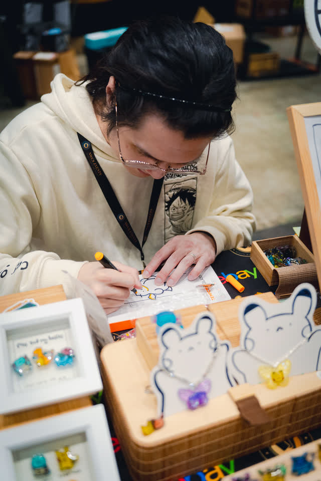 An artist sketching at a table surrounded by small framed pieces.