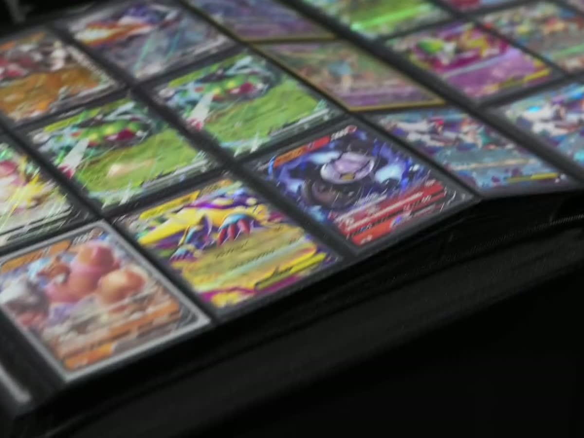 A slow pan across open binder pages of holographic cards laid out on a vendor table.