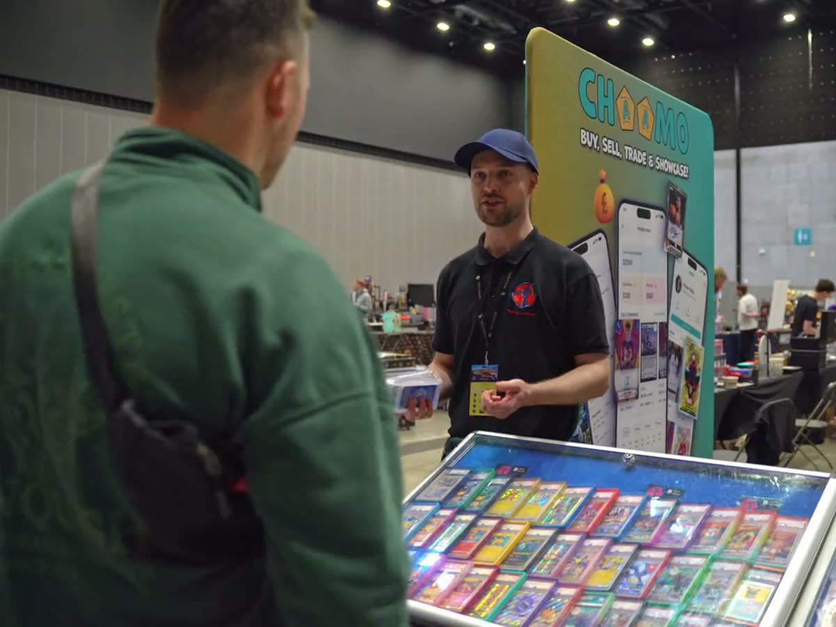 A collector talking with a trader across a case of cards at a stand.