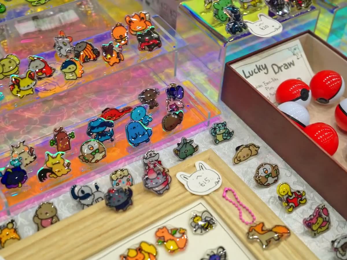 A display of enamel pins beside a lucky draw box of Poke Balls.