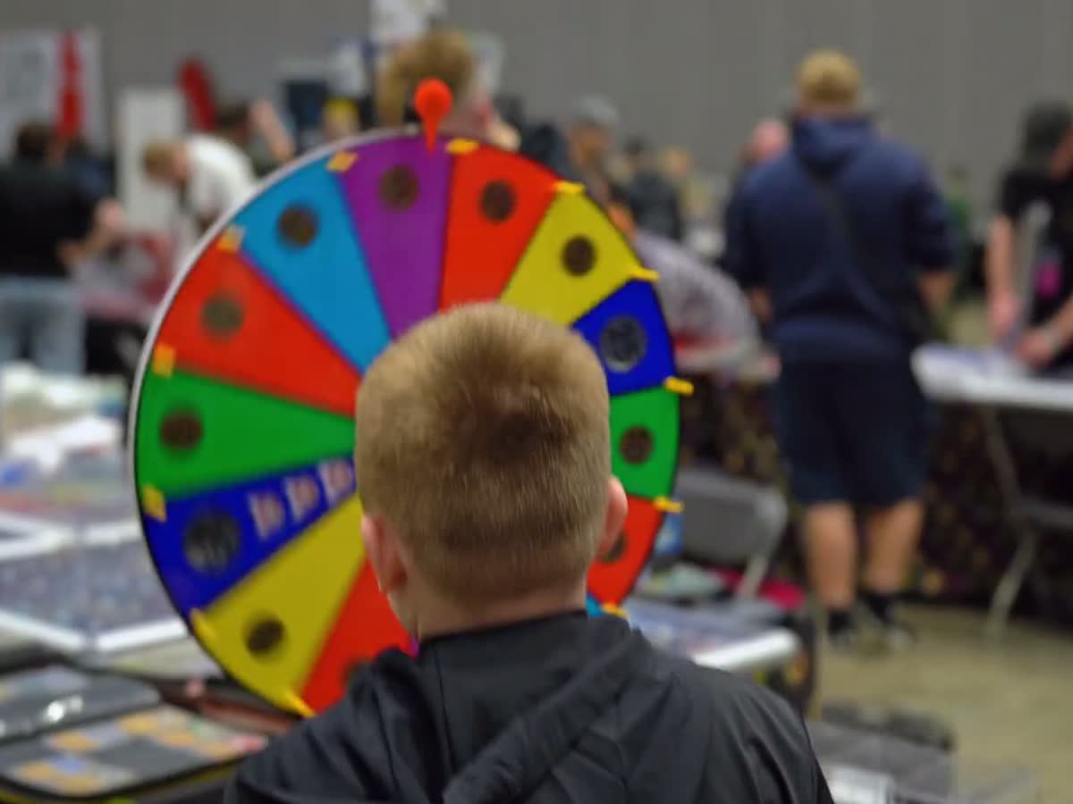 A child watching a prize wheel spin at a stand in the busy hall.